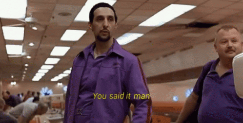 A Man In A Purple Shirt Is Standing Next To Another Man In A Bowling Alley . GIF