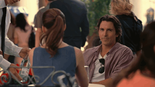 A Man In A Purple Shirt Sits At A Table Talking To A Woman GIF