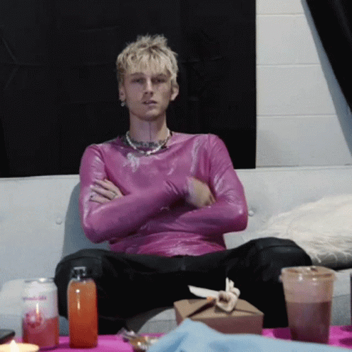 A Man In A Purple Shirt Sits On A Couch With His Arms Crossed GIF