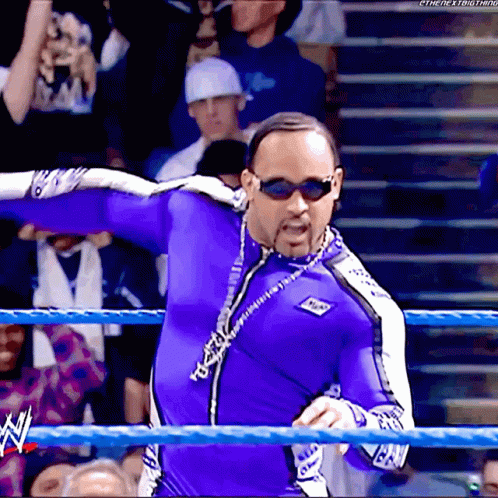 A Man In A Purple Suit And Sunglasses Stands In A Wrestling Ring With A Watermark That Says The Next Thing GIF