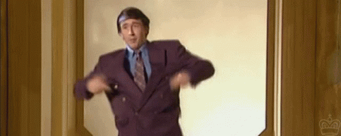 A Man In A Purple Suit And Tie Is Standing In A Doorway And Dancing . GIF