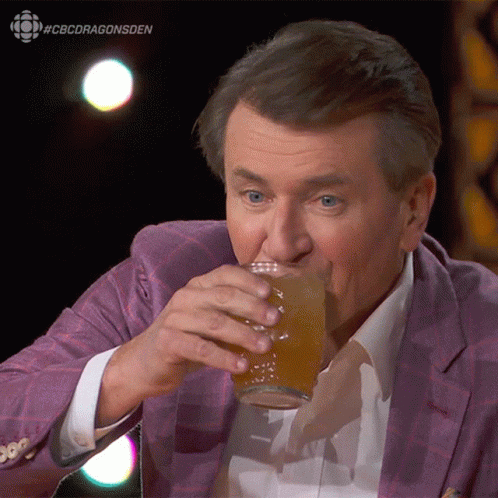 A Man In A Purple Suit Is Drinking From A Glass With #Cbcdragonsden Written On The Bottom GIF