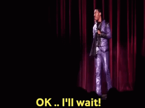 A Man In A Purple Suit Is Standing On A Stage Holding A Microphone And Saying Ok . GIF