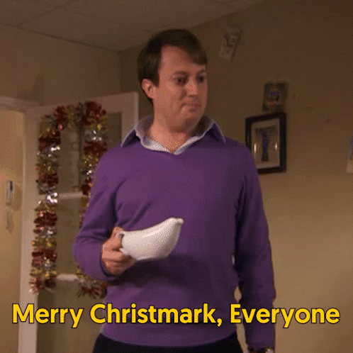 A Man In A Purple Sweater Is Holding A White Object And Says Merry Christmark Everyone GIF