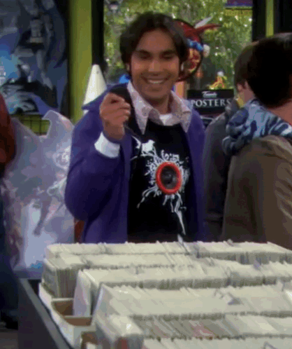 a man in a purple sweater is standing in front of a table with a sign that says posters