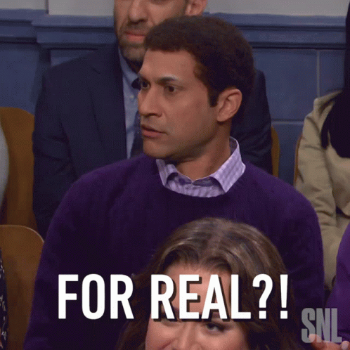A Man In A Purple Sweater Sits In Front Of A Sign That Says " What The Hell Is That Snl " GIF