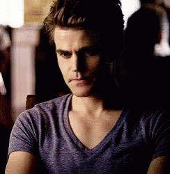 A Man In A Purple T-Shirt Is Sitting In A Dark Room . GIF