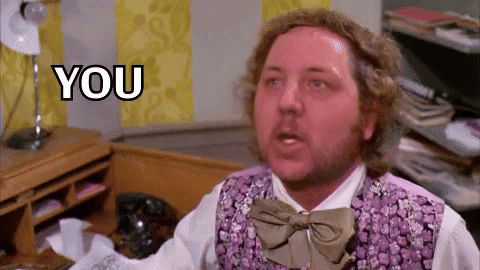 A Man In A Purple Vest And Bow Tie Is Sitting In Front Of A Desk . GIF
