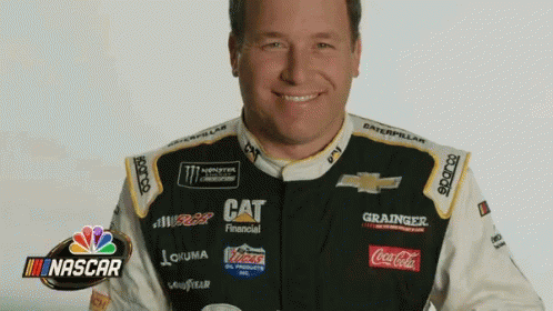 A Man In A Race Car Uniform Is Smiling With A Nascar Logo In The Background GIF