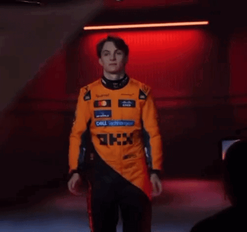 A Man In A Racing Suit Is Standing In Front Of A Red Light . GIF