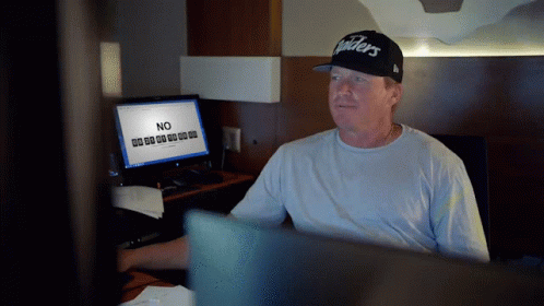 A Man In A Raiders Hat Sits In Front Of A Computer GIF