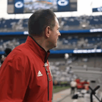 A Man In A Red Adidas Jacket Stands In Front Of A Crowd GIF