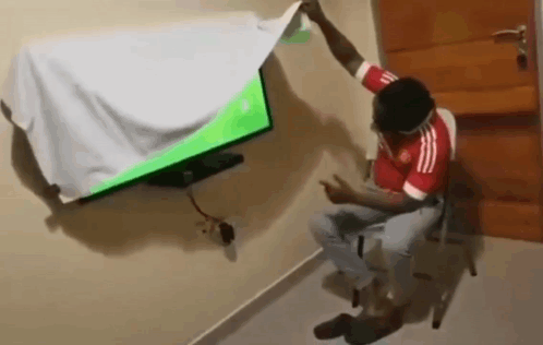 A Man In A Red Adidas Shirt Is Sitting In Front Of A Television GIF