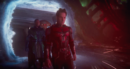 A Man In A Red And Black Costume Stands In Front Of A Portal GIF