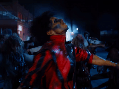 A Man In A Red And Black Jacket Is Surrounded By A Crowd Of Zombies GIF
