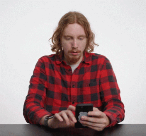 A Man In A Red And Black Plaid Shirt Is Looking At His Cell Phone GIF