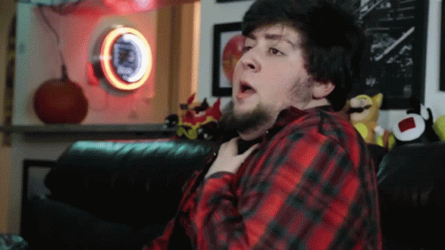 A Man In A Red And Black Plaid Shirt Is Sitting On A Couch In Front Of A Pepsi Sign GIF