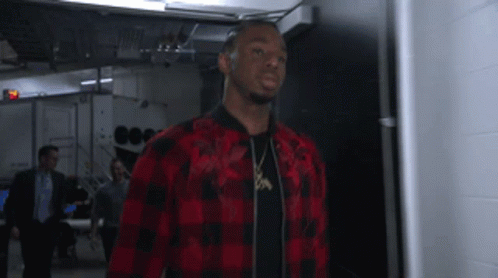 A Man In A Red And Black Plaid Shirt Is Standing In A Hallway GIF