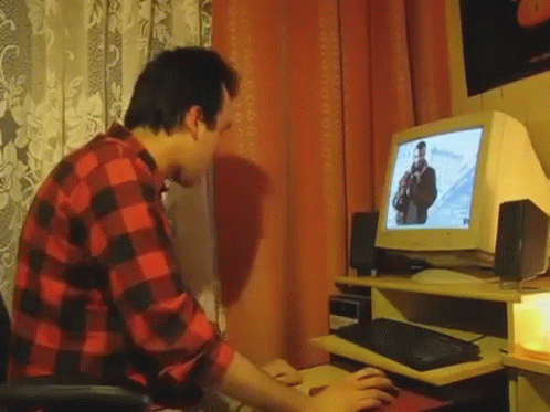 A Man In A Red And Black Plaid Shirt Is Typing On A Keyboard In Front Of A Computer Monitor . GIF