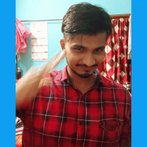 A Man In A Red And Black Plaid Shirt Stands In Front Of A Blue Wall With A Calendar On It GIF