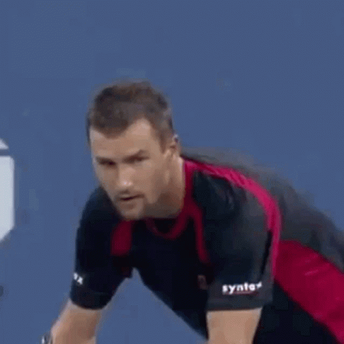 A Man In A Red And Black Shirt Is Playing Tennis On A Court . GIF