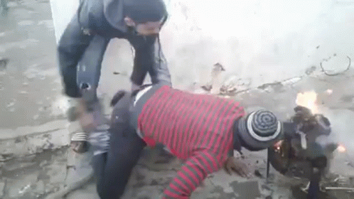 A Man In A Red And Black Striped Shirt Is Kneeling Down Next To A Fire . GIF