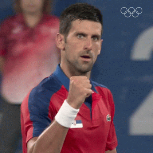 A Man In A Red And Blue Shirt Is Holding His Fist In The Air While Wearing A Wristband . GIF