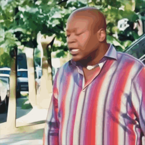 A Man In A Red And Blue Striped Shirt Stands On A Sidewalk GIF