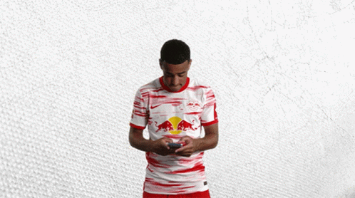 a man in a red and white red bull shirt holds a cell phone