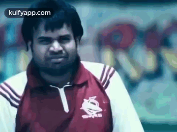 A Man In A Red And White Shirt Is Standing In Front Of A Wall With Graffiti On It . GIF