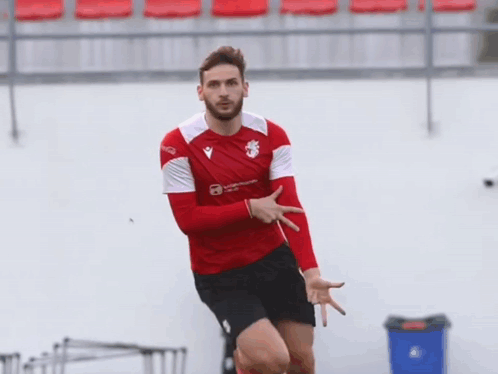 A Man In A Red And White Shirt With A Lion On It Is Pointing At Something GIF