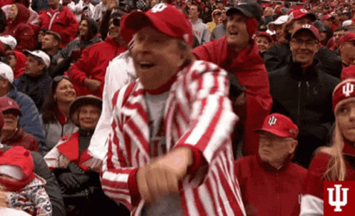 A Man In A Red And White Striped Jacket And Hat Is Dancing In A Crowd Of People . GIF
