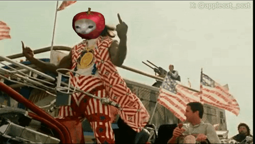 A Man In A Red And White Striped Outfit With An Apple On His Head GIF