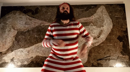 A Man In A Red And White Striped Shirt Is Dancing In Front Of A Painting GIF