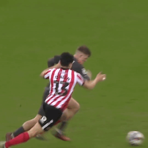 a man in a red and white striped shirt is hugging another man in a black shirt on a soccer field .
