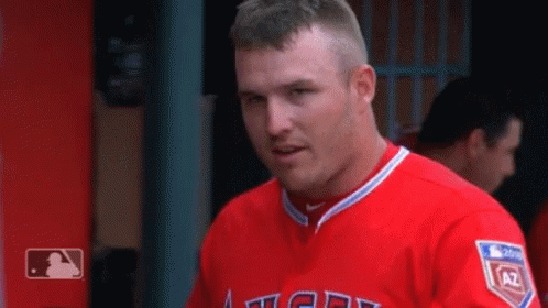 A Man In A Red Angels Jersey Is Standing In The Dugout . GIF