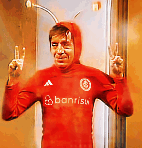 a man in a red banrisul shirt giving the peace sign
