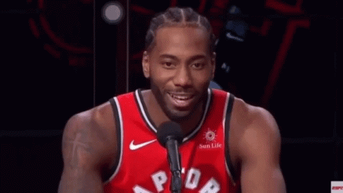 A Man In A Red Basketball Jersey Is Talking Into A Microphone . GIF