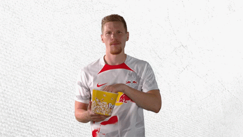 a man in a red bull shirt holds a bowl of popcorn
