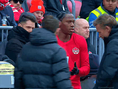 A Man In A Red Canada Shirt Stands In A Crowd Of People GIF