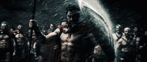 A Man In A Red Cape Is Holding A Spear And Shield In Front Of A Group Of Men GIF