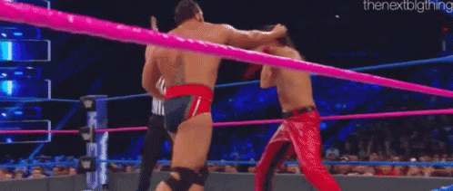 A Man In A Red Cape Is Wrestling Another Man In A Ring . GIF