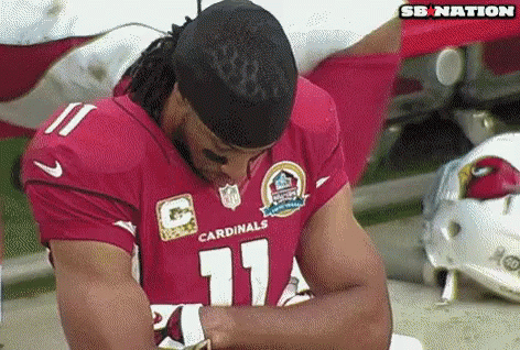 A Man In A Red Cardinals Jersey Is Sitting On The Ground With His Head Down . GIF