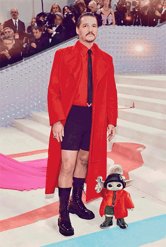 a man in a red coat and black shorts stands next to a toy