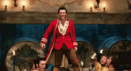 A Man In A Red Coat Is Standing On One Leg In Front Of A Group Of Men In A Room . GIF