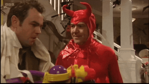 A Man In A Red Devil Costume Talks To Another Man In A White Shirt GIF