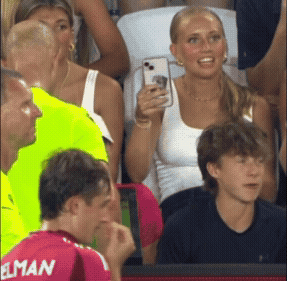 A Man In A Red Elman Jersey Looks At A Woman Taking A Picture GIF