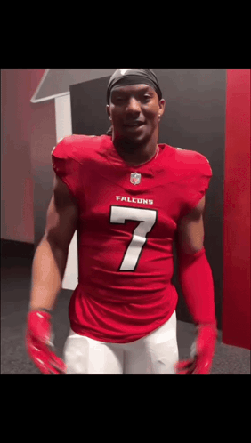 A Man In A Red Falcons Jersey Is Standing In A Locker Room GIF