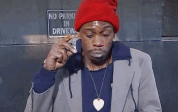 A Man In A Red Hat Is Eating A Sandwich In Front Of A No Parking Sign GIF
