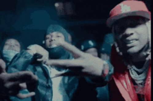 A Man In A Red Hat Is Making A Peace Sign In Front Of A Group Of People . GIF